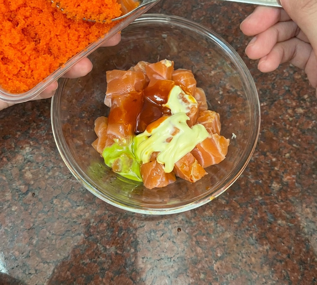Une cuillère en argent déposant des œufs de poisson orange vif sur le saumon en cubes.