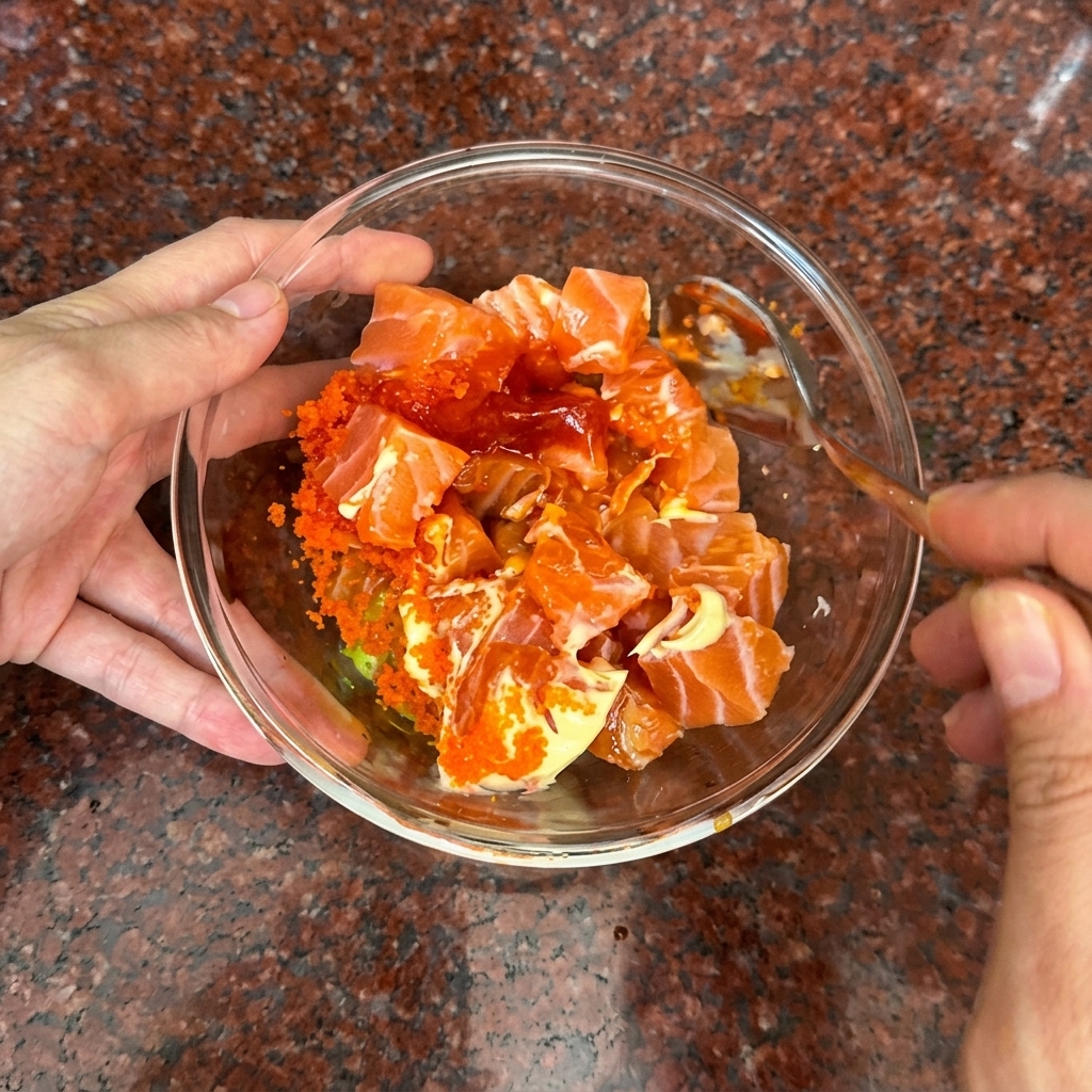 Une main mélangeant délicatement les cubes de saumon et la sauce orange à la cuillère.
