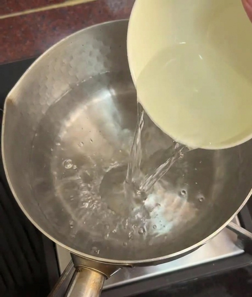 Une personne versant un bol deau froide dans une casserole deau bouillante hors du feu.