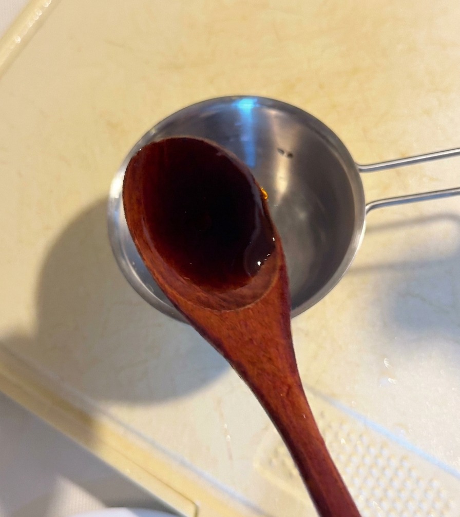 Une cuillère en bois versant de la sauce dhuître foncée dans un petit bol de préparation contenant les ingrédients de la sauce.