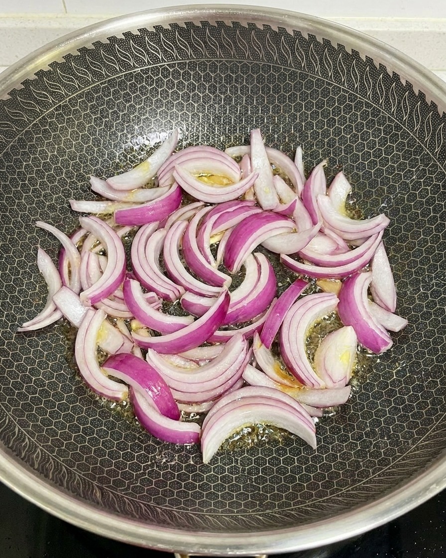 Des lamelles doignon rouge sautées dans un wok chaud aux motifs hexagonaux avec un filet dhuile luisante.
