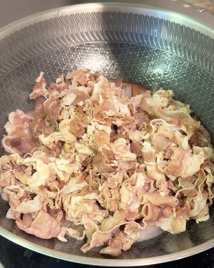 De tendres lamelles de bœuf blanchies mélangées à des oignons rouges et à une sauce foncée dans un wok en acier inoxydable.