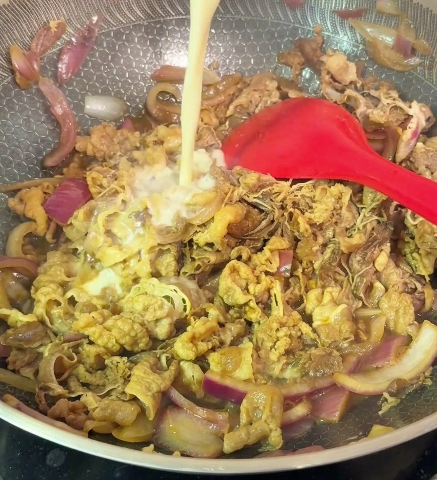 Un filet de fécule diluée de couleur pâle versé dans un wok aux motifs hexagonaux rempli de bœuf sauté et doignons rouges.