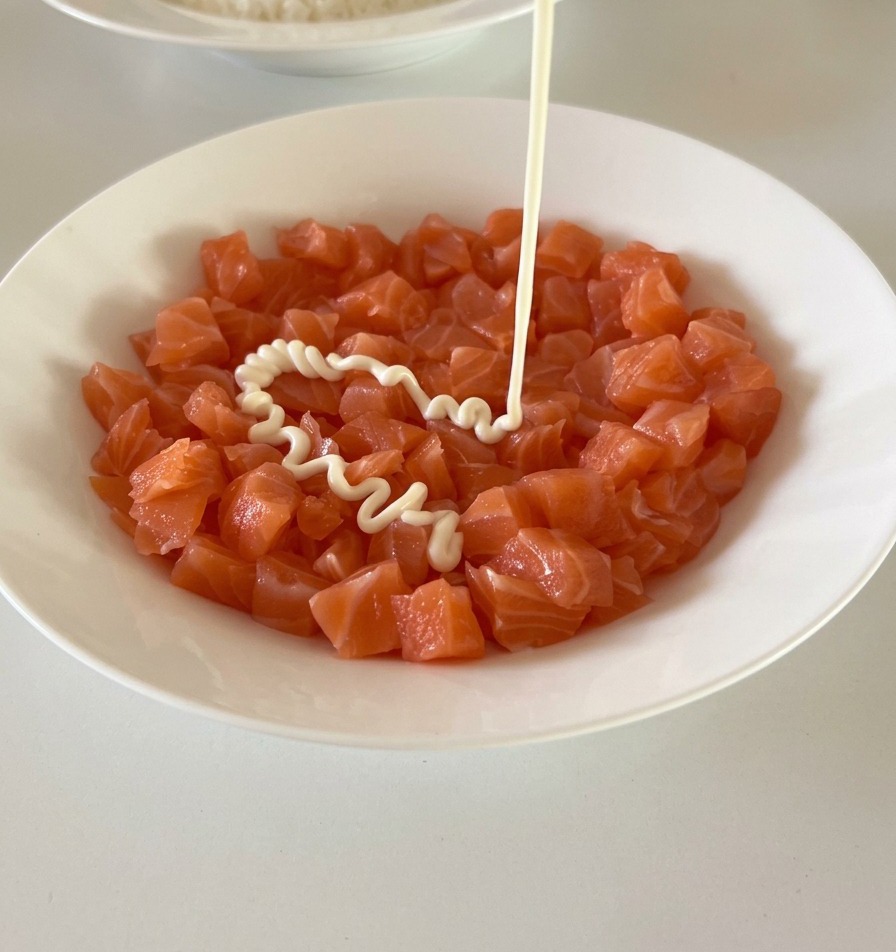 De la mayonnaise blanche et onctueuse versée depuis un flacon sur un bol de dés de saumon frais et orangé.
