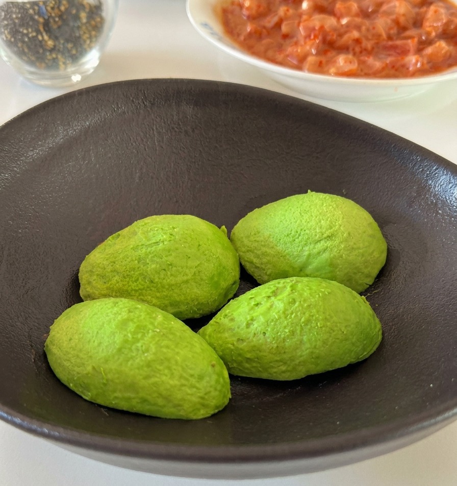 Une main pressant un quartier de citron frais au-dessus de moitiés davocat vert dans un bol en céramique.