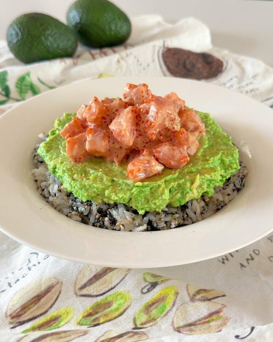 Un poke bowl révélant des couches superposées de riz assaisonné, davocat écrasé et de cubes de saumon crémeux.