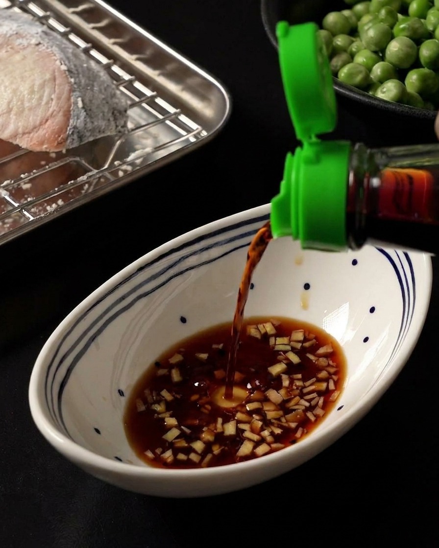 De la sauce soja foncée versée dans un bol blanc contenant une base de gingembre émincé et de miel.