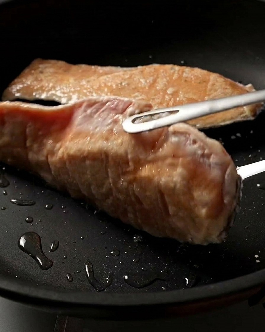 Gros plan sur un pavé de saumon que lon retourne dans la poêle, révélant une surface parfaitement dorée et croustillante.