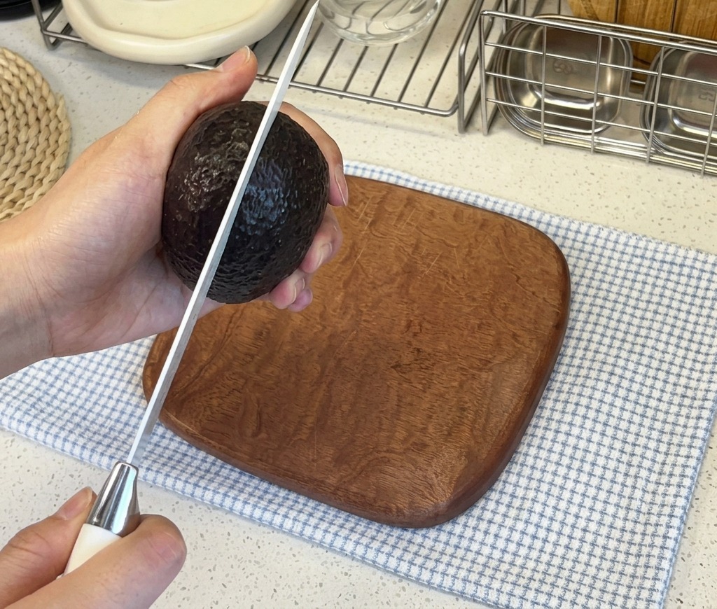 Mains coupant verticalement un avocat à la peau sombre avec un couteau de cuisine bien aiguisé.