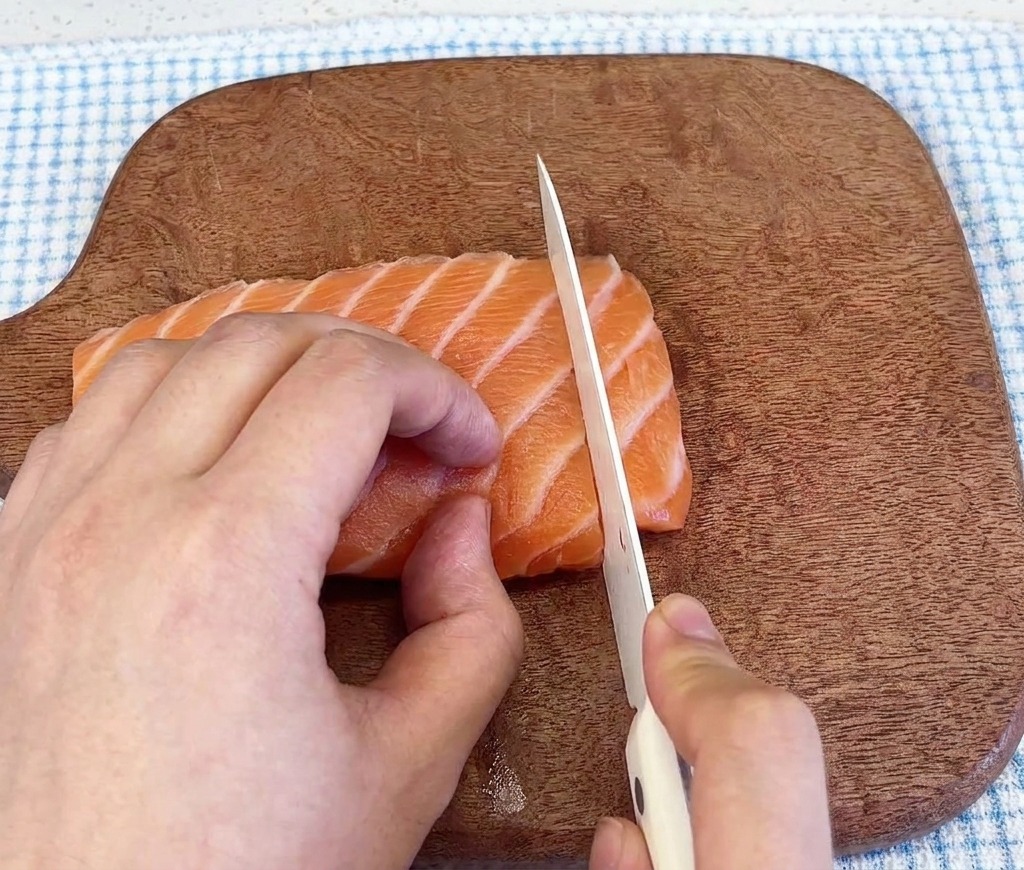 Gros plan dun couteau tranchant un filet de saumon frais et marbré sur une planche à découper en bois sombre.