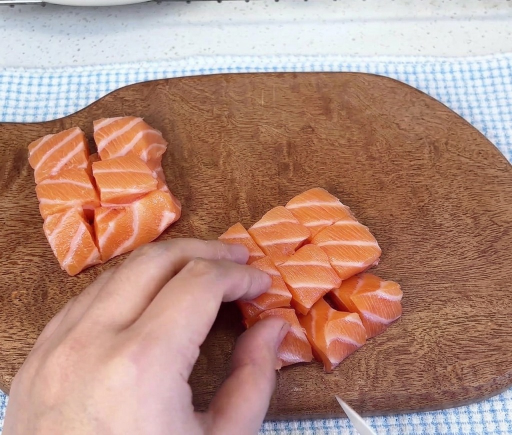 Plusieurs petits tas de saumon cru coupés en dés reposant sur une planche à découper en bois.
