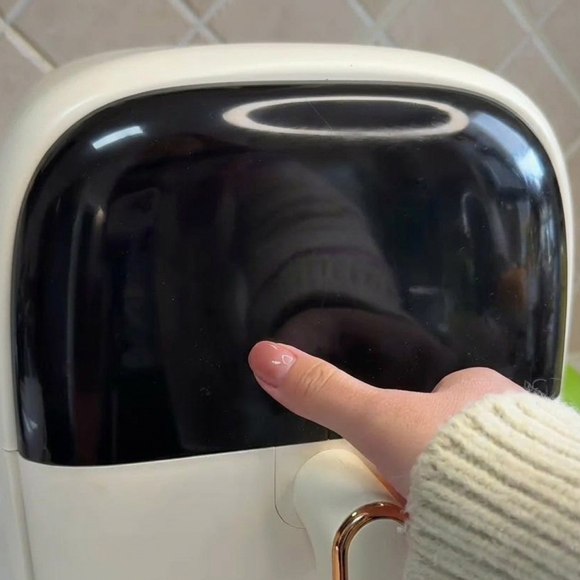 Gros plan dune main touchant le panneau de commande tactile noir dun air fryer blanc.