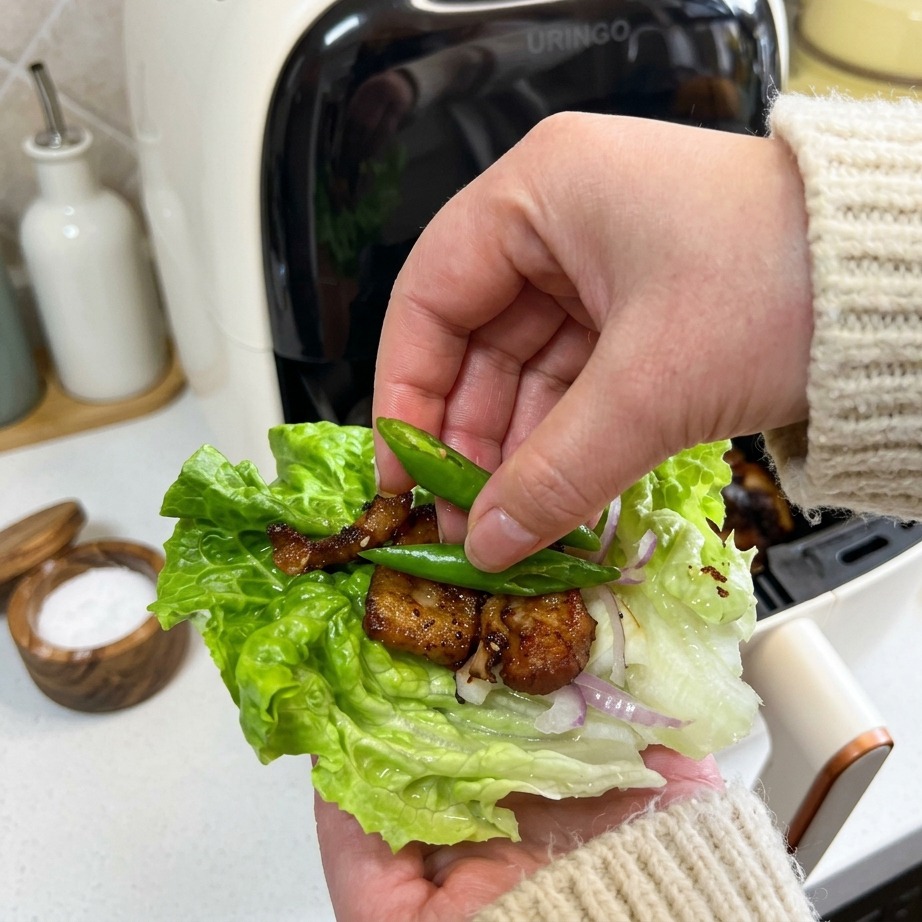 Une main déposant deux petites rondelles de piment vert frais sur un wrap de salade contenant le porc croustillant.