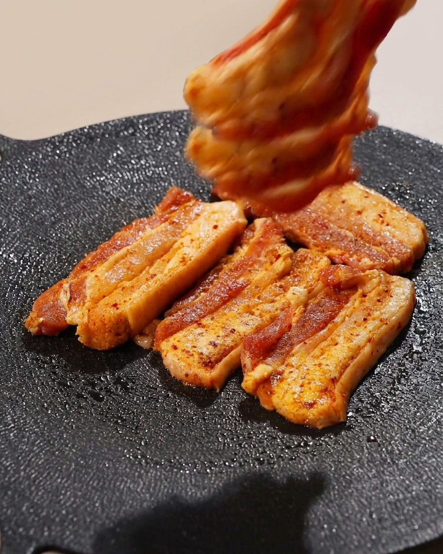 Plusieurs tranches de poitrine de porc assaisonnées disposées sur un gril chaud.