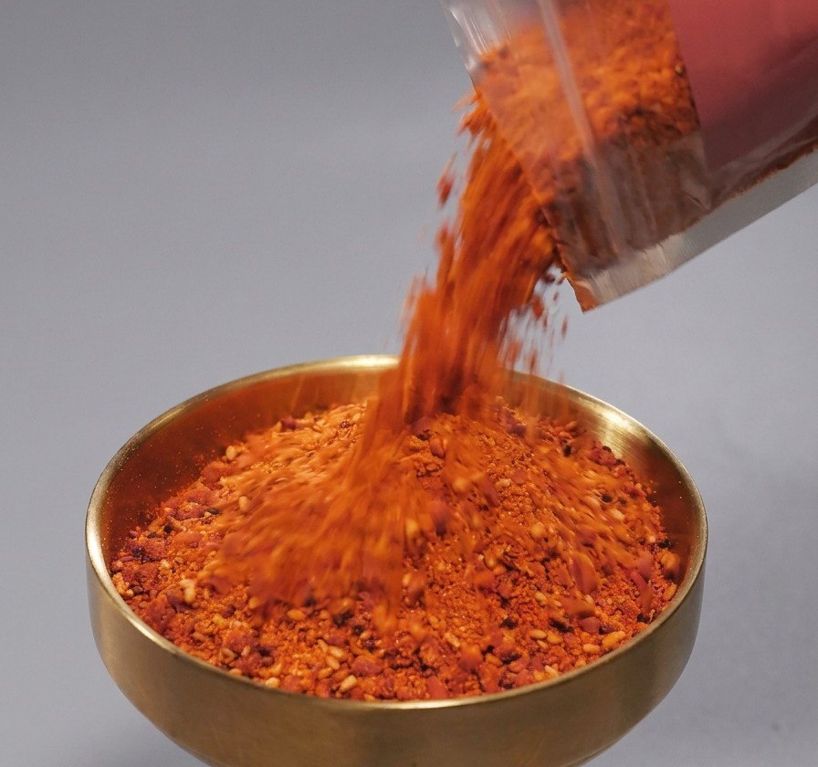 Poudre dépices rouges avec des graines de sésame versée dans un bol doré.