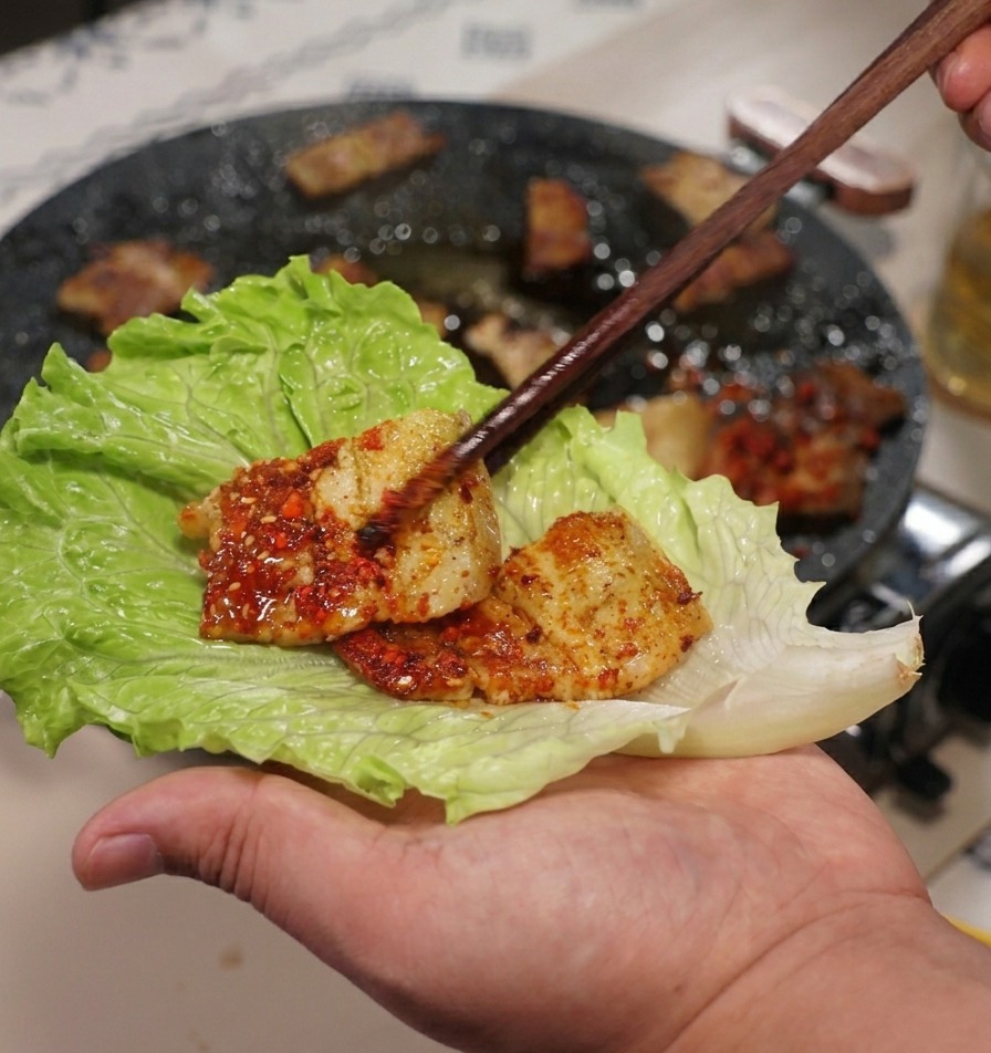 Une main tenant une grande feuille de laitue verte tout en y déposant un morceau de poitrine de porc.