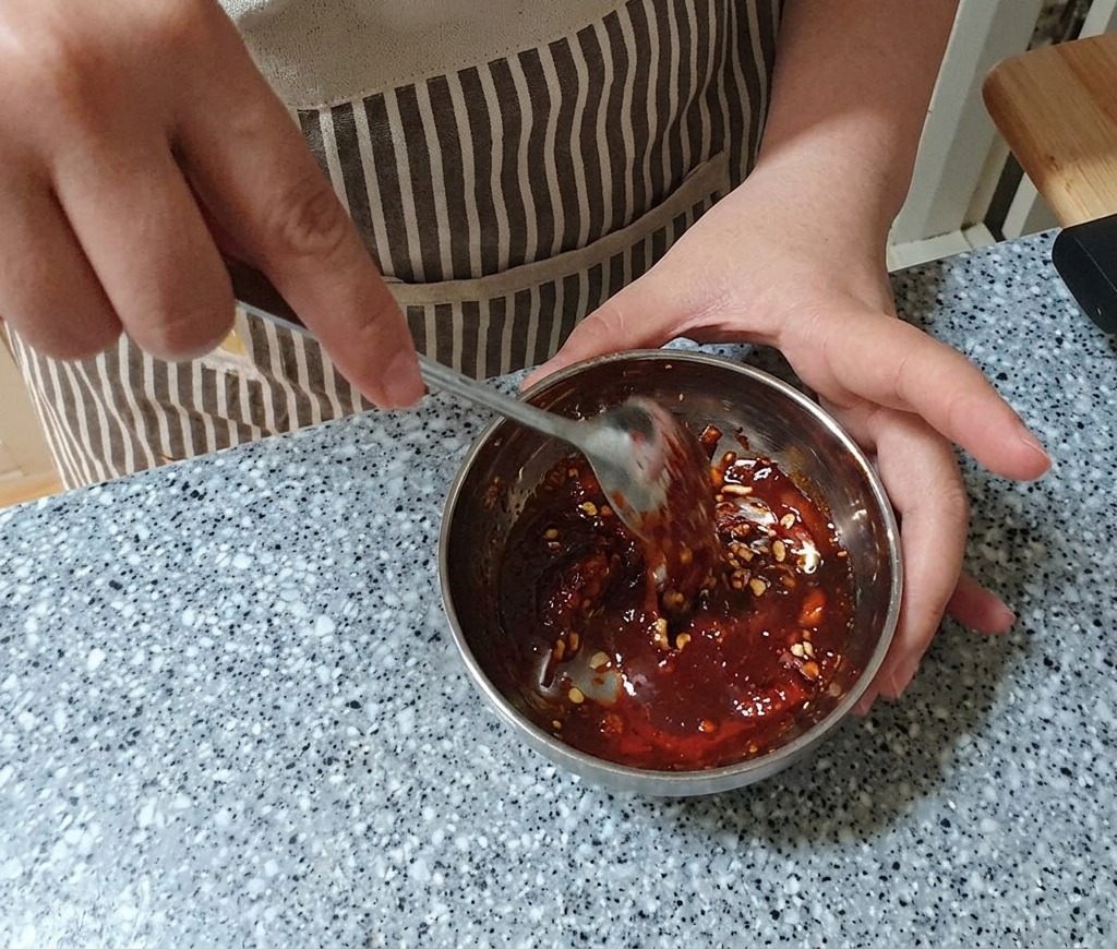 Mélange dune marinade rouge épaisse dans un bol en métal à laide dune cuillère en acier inoxydable.
