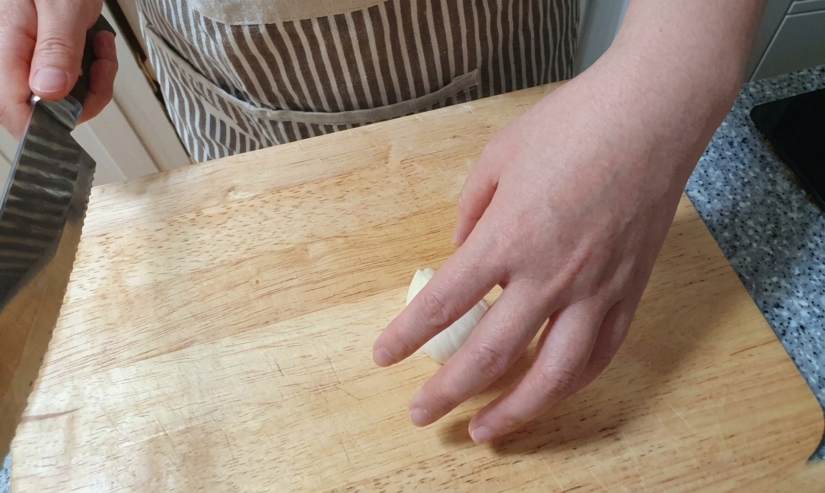Découpe de fines lamelles verticales dun oignon blanc sur une surface en bois à laide dun couteau.