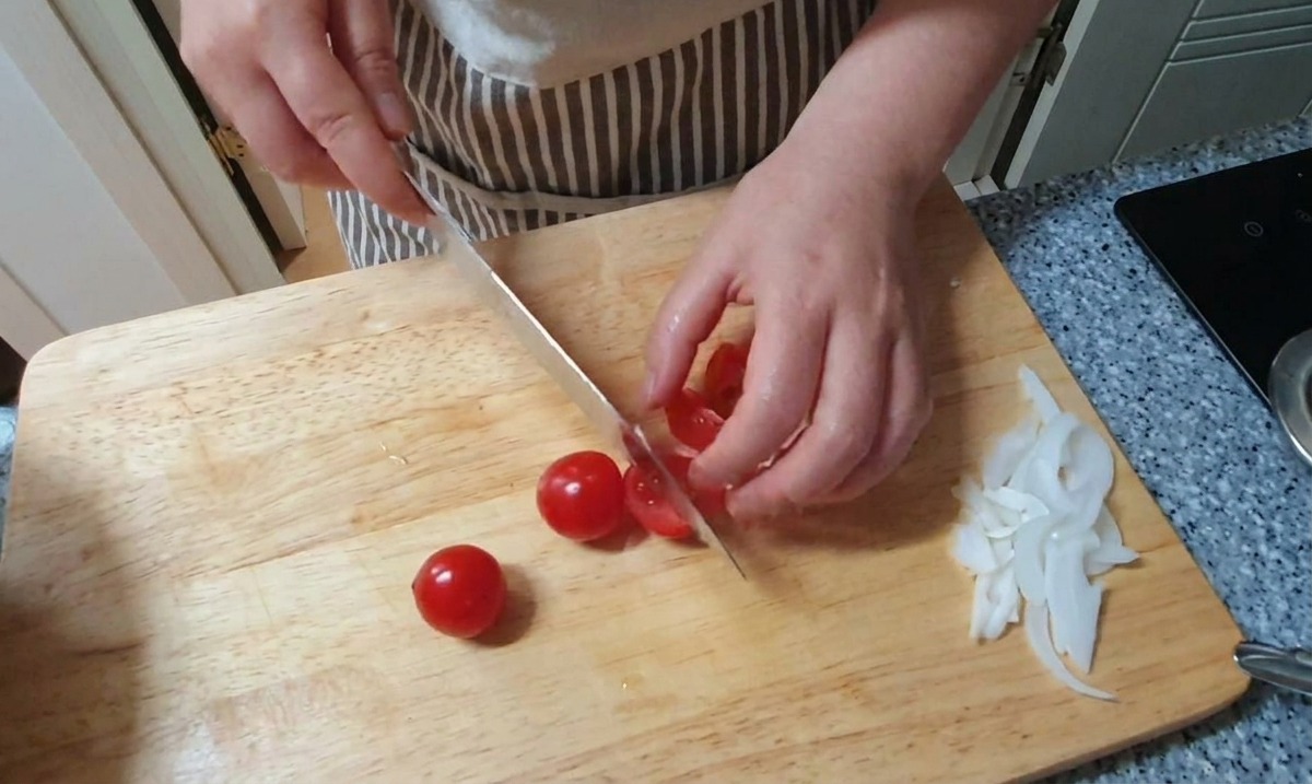 Tomates cerises rouges coupées en deux sur une planche en bois à côté dun tas doignons blancs émincés.