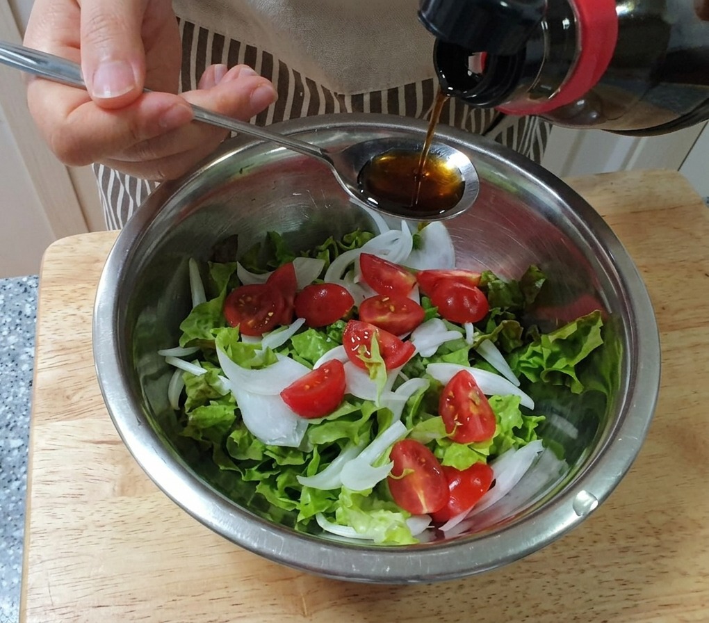 De la vinaigrette versée depuis une cuillère sur un bol de laitue, doignons et de tomates cerises.