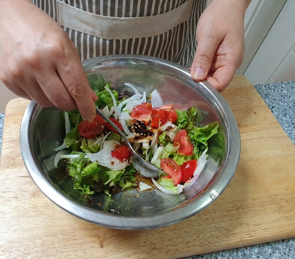 Une main mélangeant une salade de légumes frais avec une cuillère dans un grand bol en acier inoxydable.