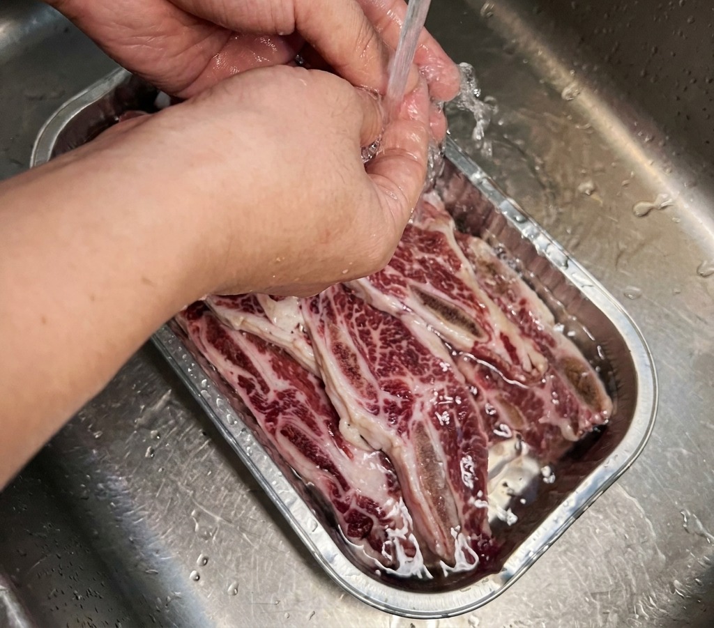 Travers de bœuf immergés dans un plateau métallique en train dêtre rempli deau froide et claire par un robinet.
