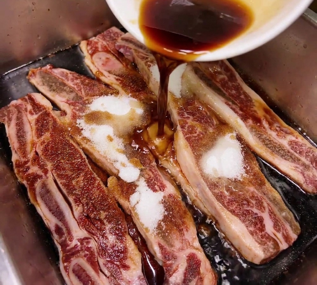 Sauce soja foncée ou mirin versé dun bol blanc sur des travers de bœuf crus saupoudrés de sucre blanc dans un plateau métallique.