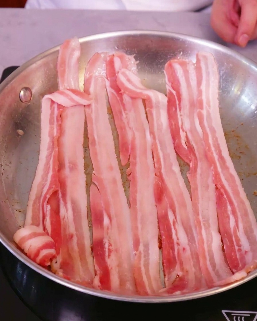 Tranches de poitrine de porc fraîche disposées dans une grande poêle en acier inoxydable sur une plaque à induction.