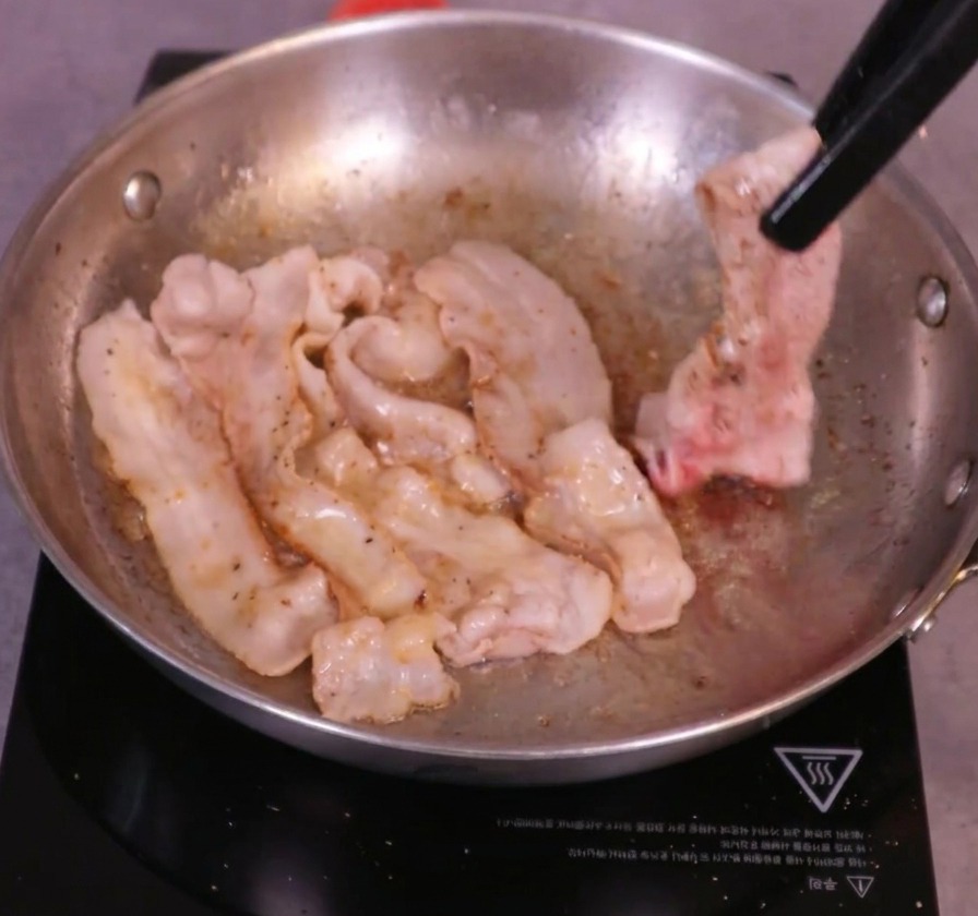 Tranches de poitrine de porc bien dorées retournées à laide dune pince de cuisine dans une poêle crépitante.