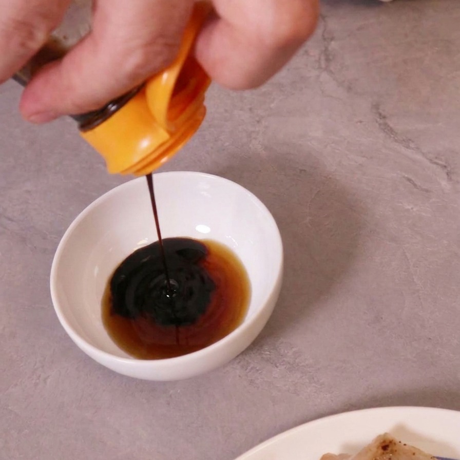 Sauce soja foncée versée dans un bol blanc contenant un liquide plus clair pour faire une sauce de trempette.