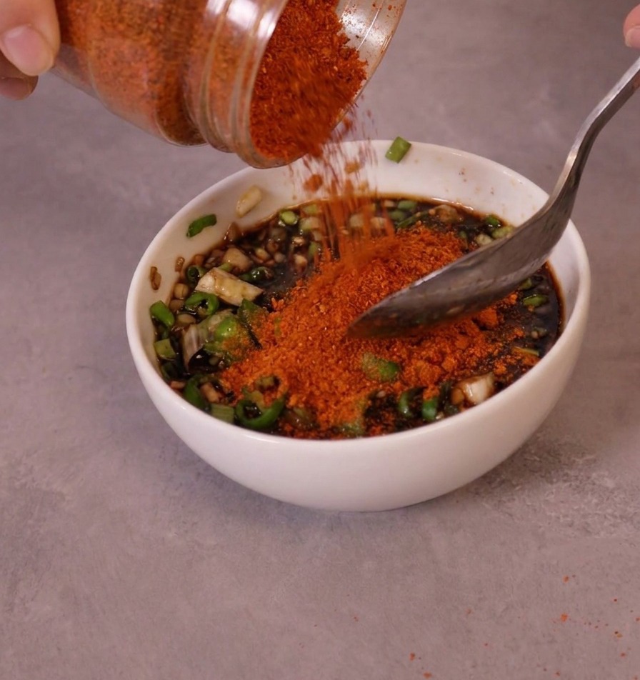 Piment rouge fin en poudre versé dun pot dans un bol de sauce préparée avec des piments verts.