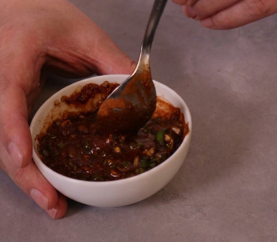 Sauce de trempette rouge épaisse et piquante remuée avec une cuillère en métal dans un petit bol en céramique.