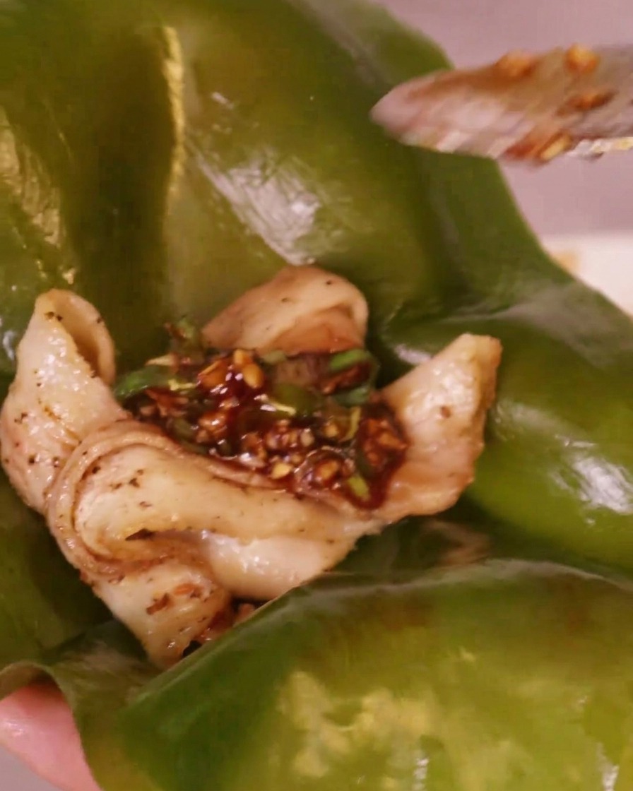 Sauce rouge piquante déposée sur un morceau de poitrine de porc grillée reposant sur une feuille de varech verte.