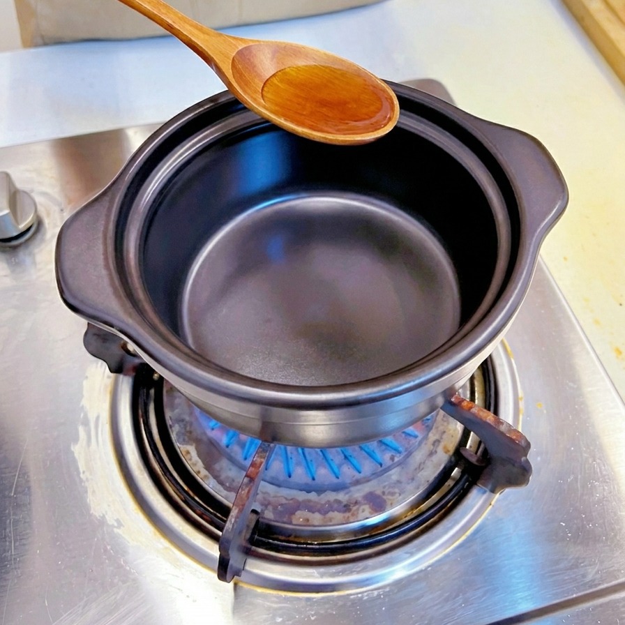 Une cuillère en bois versant de lhuile de sésame dorée dans une marmite traditionnelle en pierre noire sur une cuisinière à gaz.