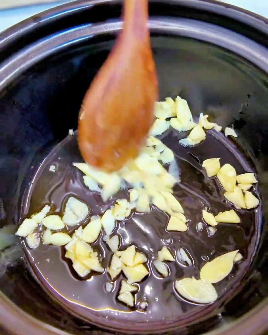 De lail émincé remué dans de lhuile de sésame au fond dune marmite noire à laide dune cuillère en bois.