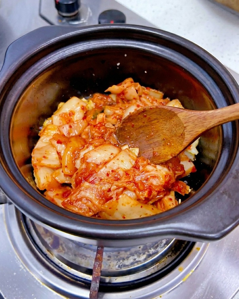 Une portion de kimchi de chou rouge haché ajoutée dans une marmite avec de lail sauté.