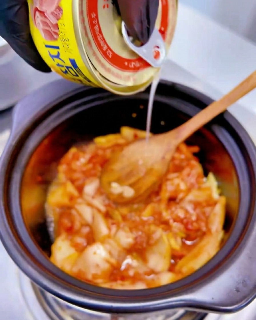 Le liquide dune boîte de thon jaune versé sur le mélange de kimchi dans la marmite.