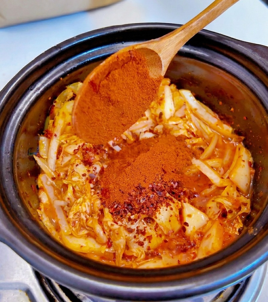 Du piment fin en poudre rouge ajouté depuis une cuillère en bois sur le mélange de kimchi et doignons assaisonné.