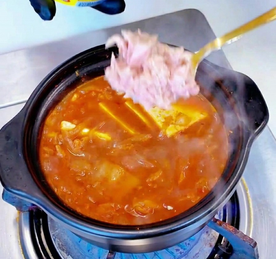 Des morceaux de thon en conserve rose clair ajoutés à la cuillère au centre dun ragoût rouge frémissant.