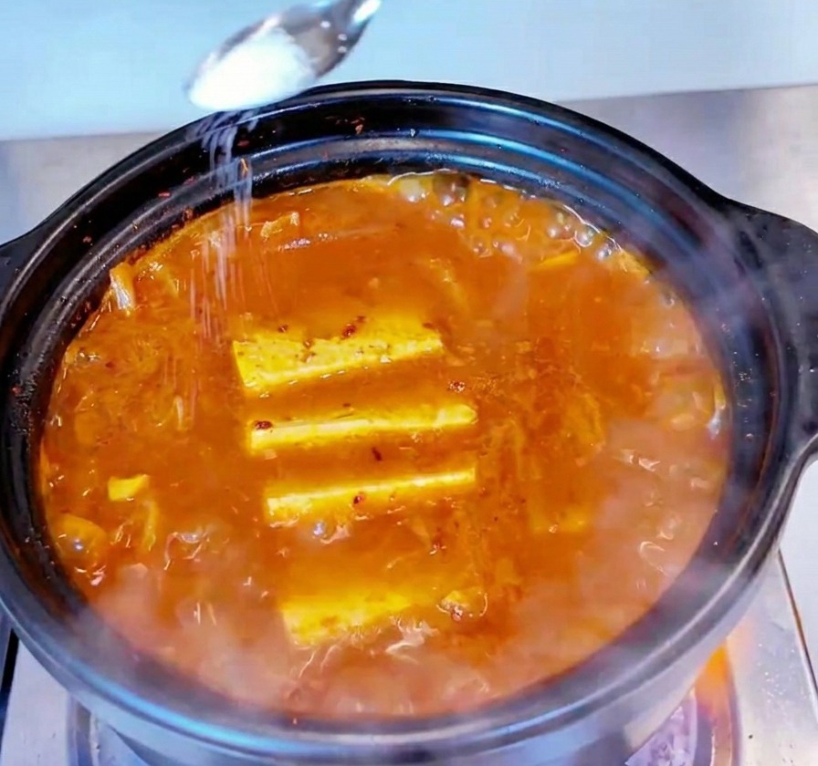 Une petite cuillère en métal saupoudrant du sel blanc sur la surface dun ragoût de kimchi au thon bouillonnant.