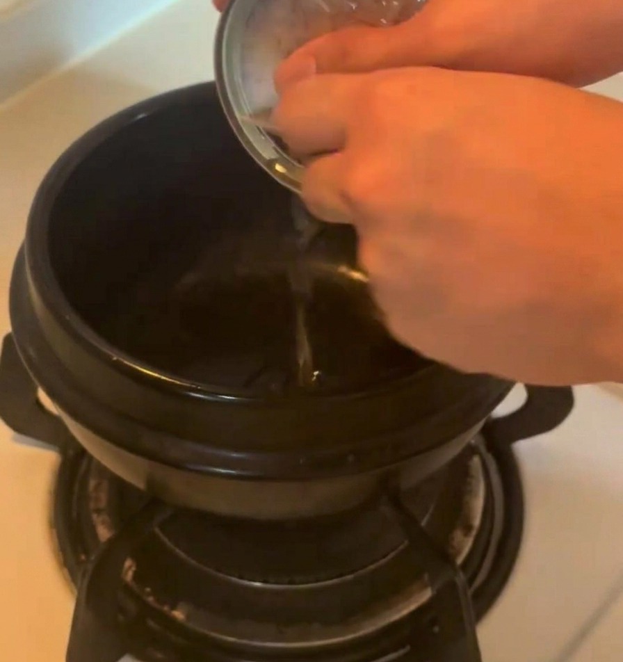 De lhuile savoureuse versée depuis une boîte de thon en métal dans une marmite en céramique noire sur un réchaud.