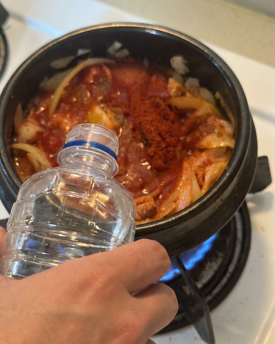 De leau versée depuis une bouteille en plastique transparent dans une marmite remplie de kimchi et de thon bien relevés.
