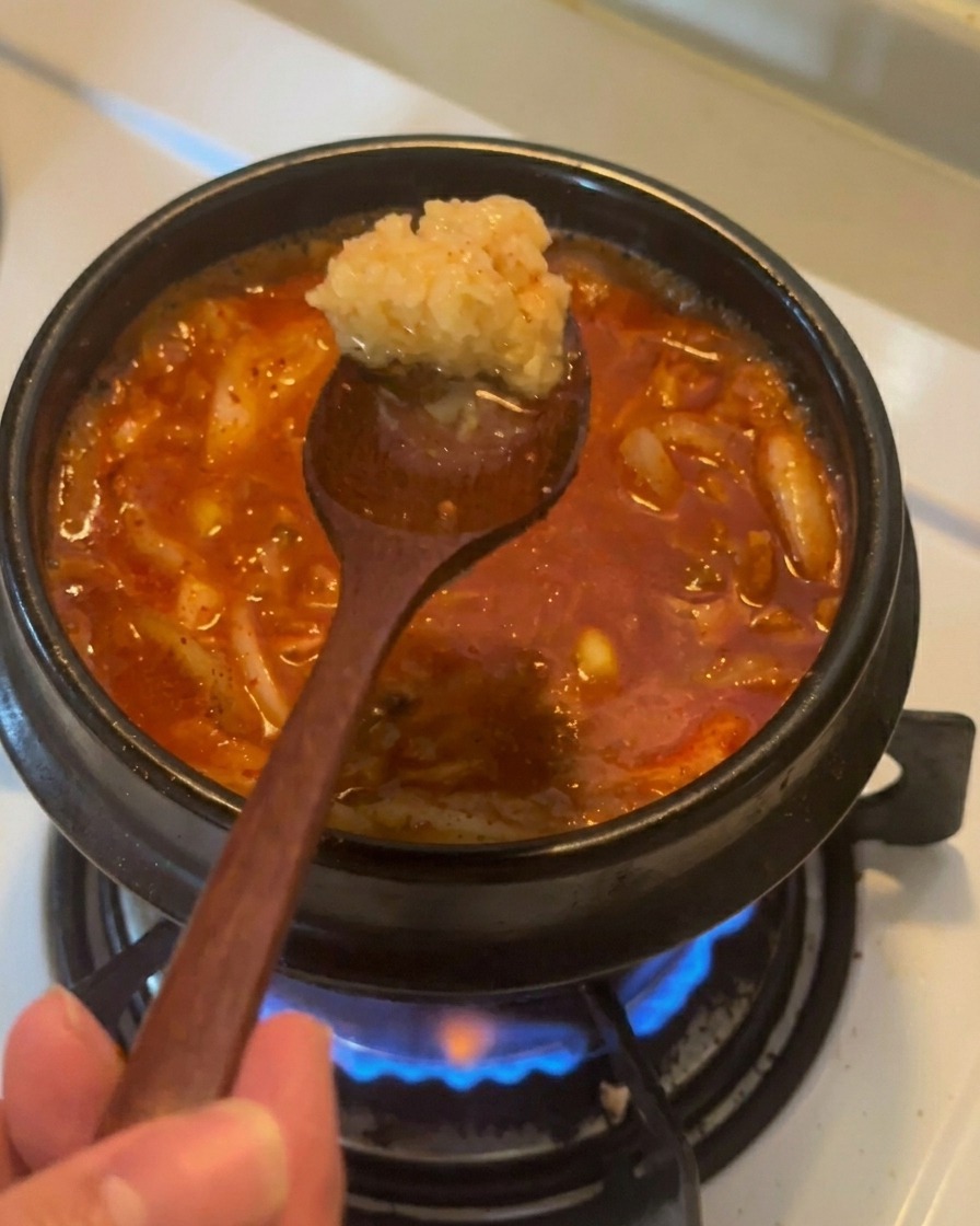 Une cuillère en bois retenant de lail haché au-dessus dun ragoût de kimchi au thon rouge et bouillonnant.