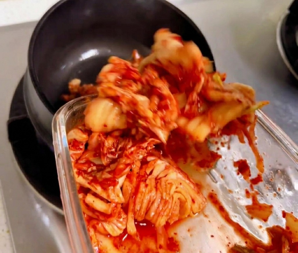 Morceaux de kimchi remués et sautés dans un pot en pierre traditionnel noir sur une flamme de gaz.
