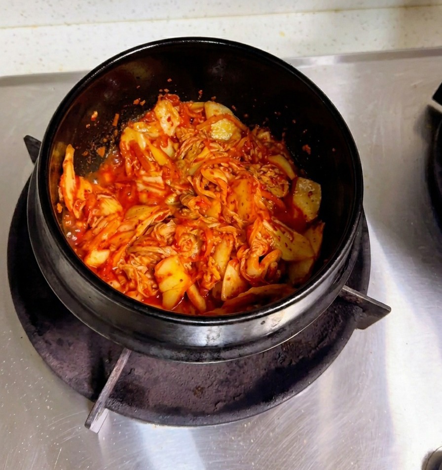 Une main versant de leau de riz trouble dans un faitout en pierre rempli de kimchi sauté.