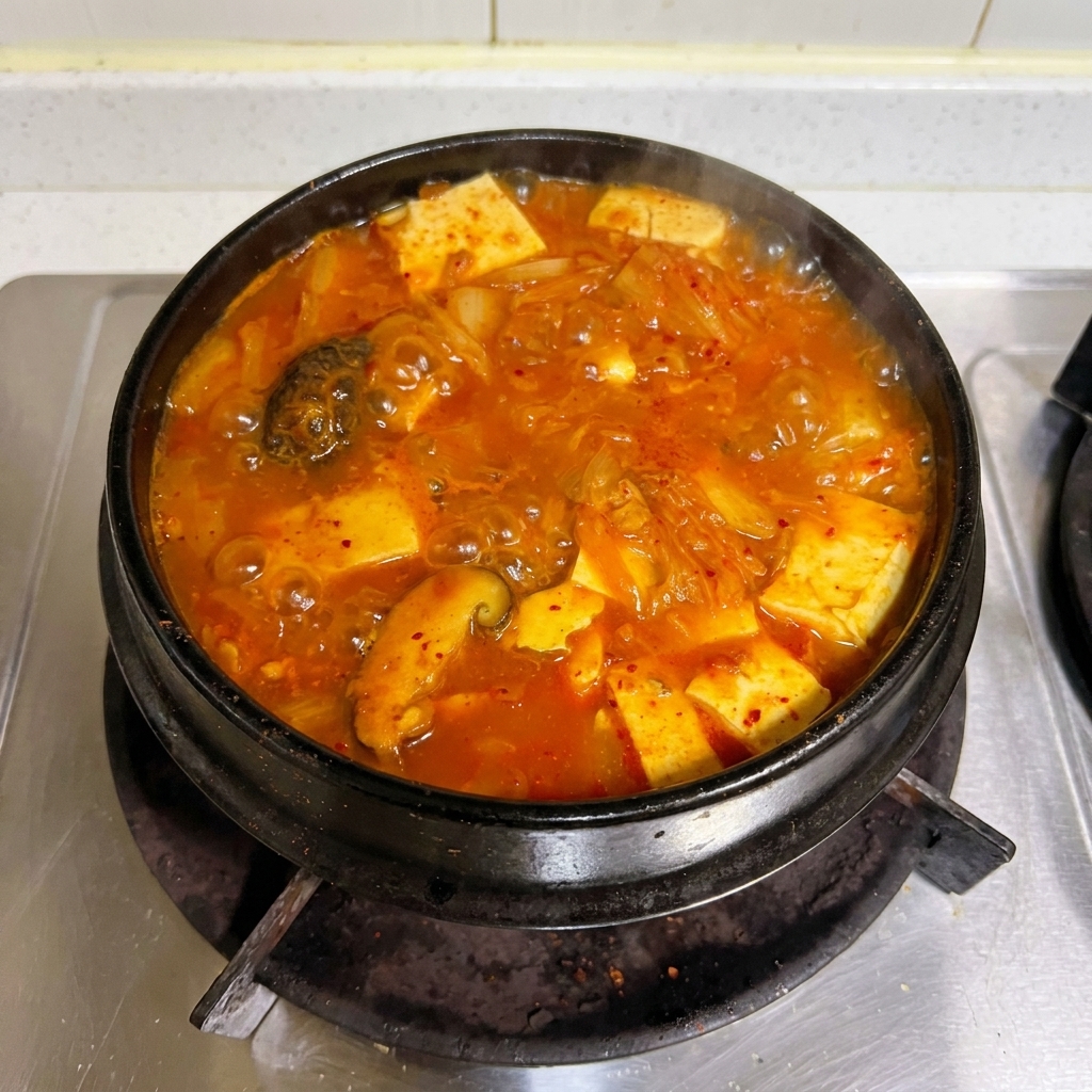 Un ragoût de kimchi et de thon rouge vif bouillant vigoureusement dans un pot en pierre traditionnel sur la cuisinière.