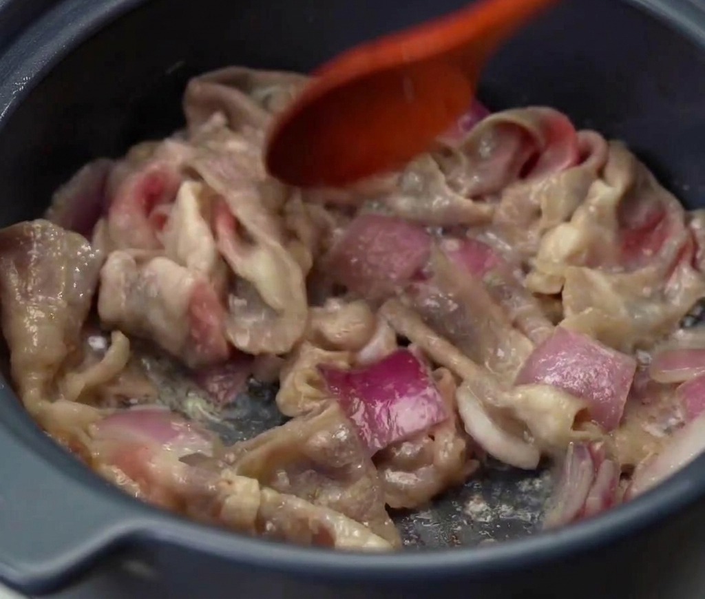 Des tranches de bœuf et des oignons rouges saisis ensemble dans une marmite jusquà ce que la viande soit cuite et colorée.