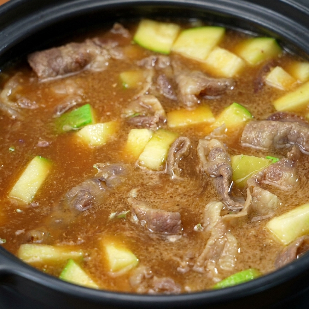 La pâte de soja se mélangeant et se dissolvant dans la marmite, transformant le liquide en un bouillon brun et trouble avec des morceaux de bœuf et de courgette visibles.
