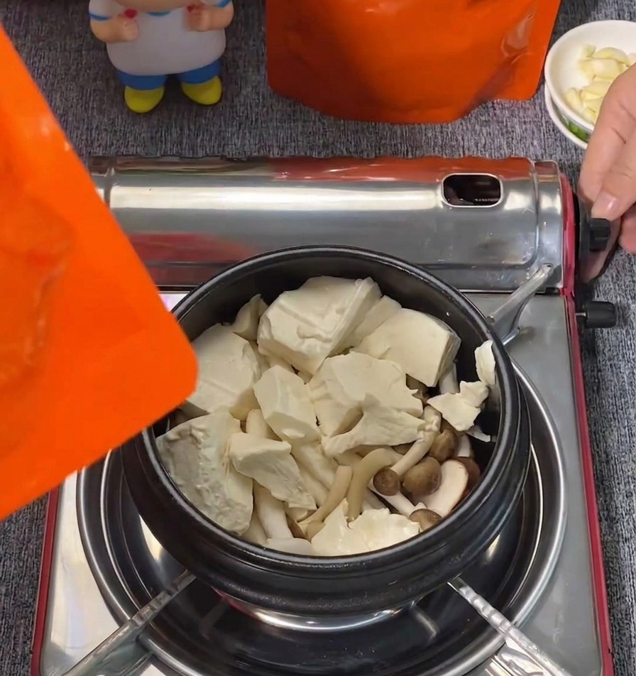 Gros blocs de tofu soyeux blanc et champignons shimeji disposés dans une marmite noire.