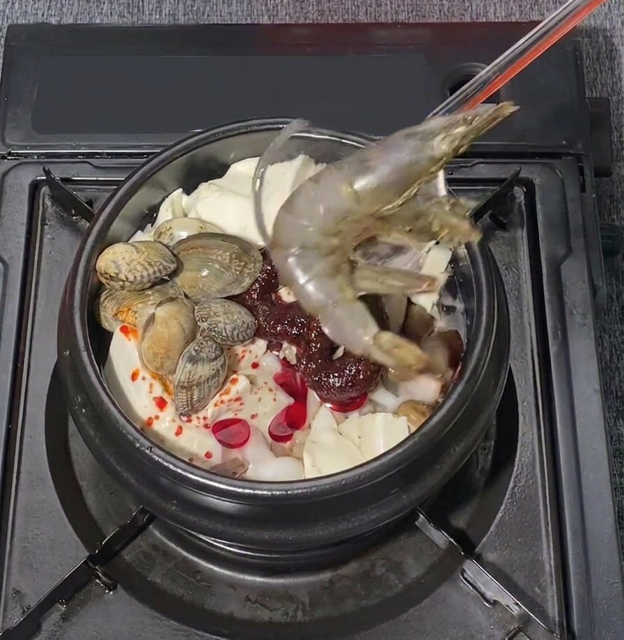Deux grandes crevettes crues délicatement placées dans une marmite frémissante de ragoût de tofu soyeux coréen aux fruits de mer.